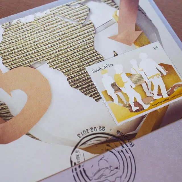 A first-day cover at an angle. A B5 stamp showing four white paper-cutout rescuers carrying a stretcher sits on an envelope illustrated with a corrugated-card continent, a torn paper arrow and a Pretoria postmark dated 22.02.2013.